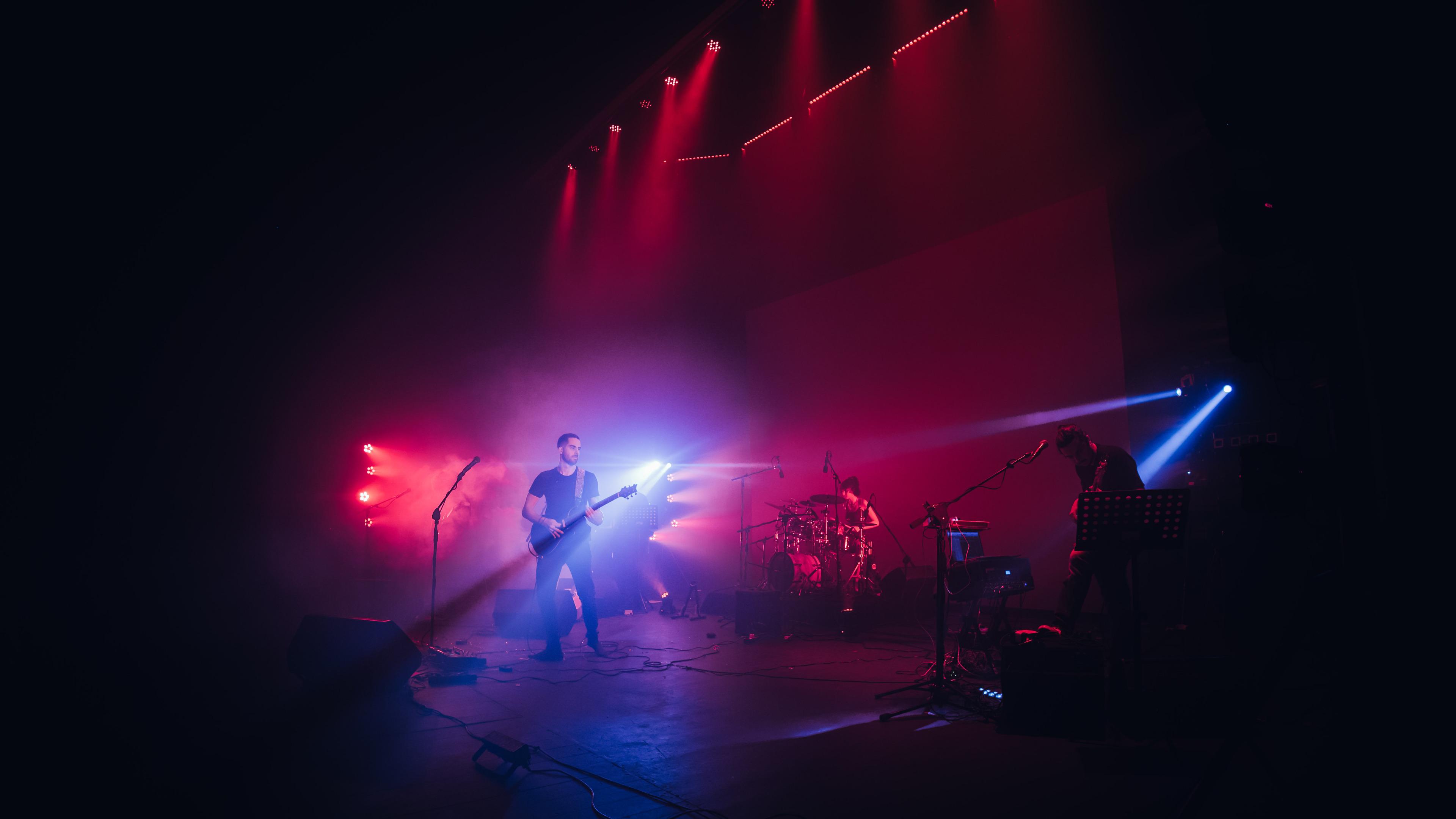 Picture of a band on stage with many fluorescent lights surrounding them promoting artist submissions on MusicLeb so that they can easily found and looked into.